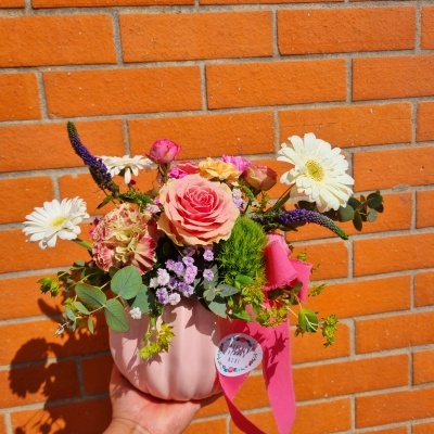 Vaso rosa com arranjo de flores coloridas contra parede de tijolos laranja