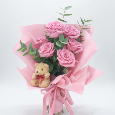 Buquê de rosas cor-de-rosa com papel e fitas cor-de-rosa e ursinho de pelúcia.