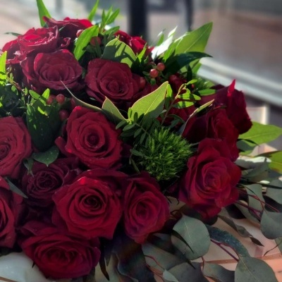 Buquê de rosas vermelhas com folhas verdes e frutos pequenos, em papel de embrulho