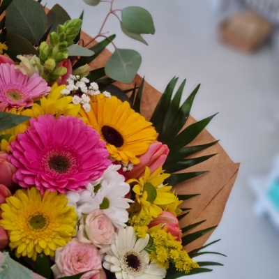 Ramo colorido de flores com várias espécies e folhagem, embrulhado em papel castanho