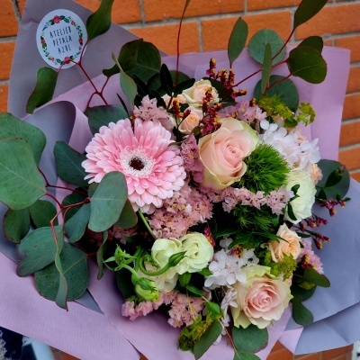 Buquê de flores variadas com papel lilás e etiqueta redonda em fundo de parede tijolos