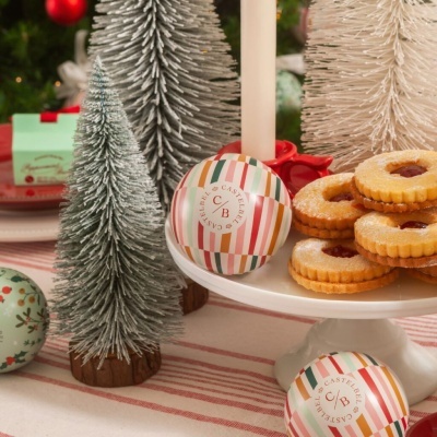 Bolas decorativas listradas, árvores artificiais e biscoitos recheados sobre toalha riscada