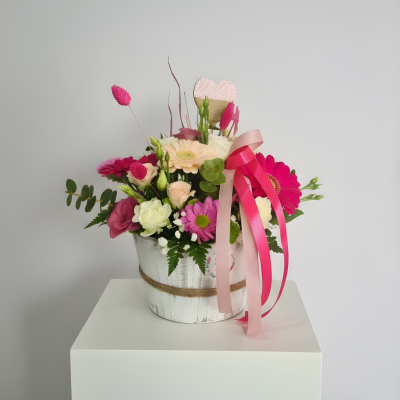 Arranjo floral colorido em vaso branco com fitas rosas e coração decorativo