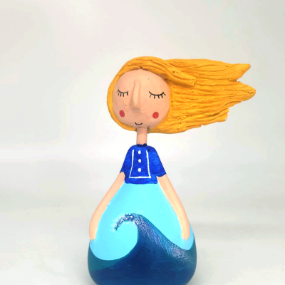 Figura decorativa de menina com cabelo amarelo e vestido azul com padrão de onda