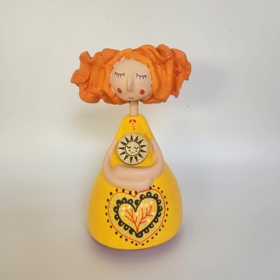 Boneca decorativa amarela com cabelo laranja e detalhe do sol dourado