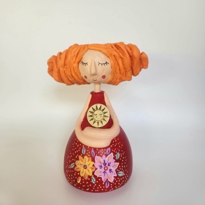 Boneca de madeira decorativa com cabelo laranja e vestido vermelho com flores.