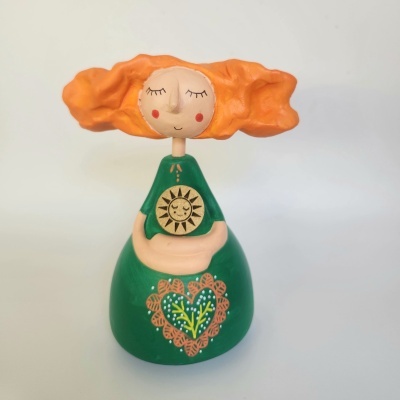 Estatueta decorativa de mulher com cabelo alaranjado e vestido verde com sol dourado desenhado