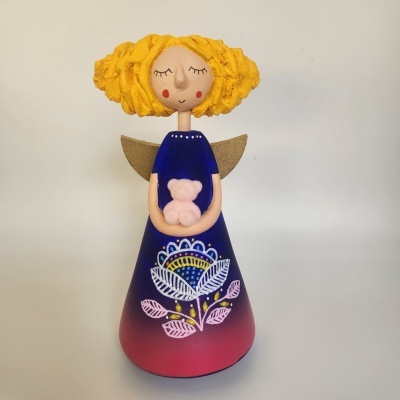Figura decorativa em madeira com vestido azul e padrão floral, cabelo amarelo e ursinho cor-de-rosa