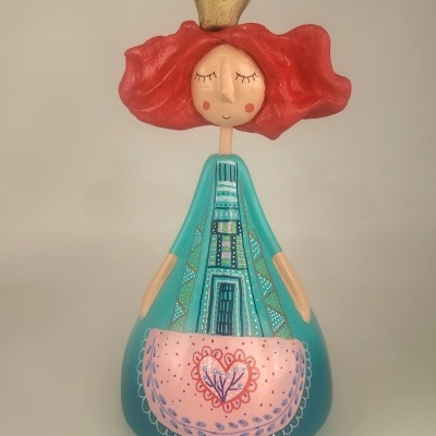 Boneca decorativa azul-turquesa com avental rosa e coroa dourada