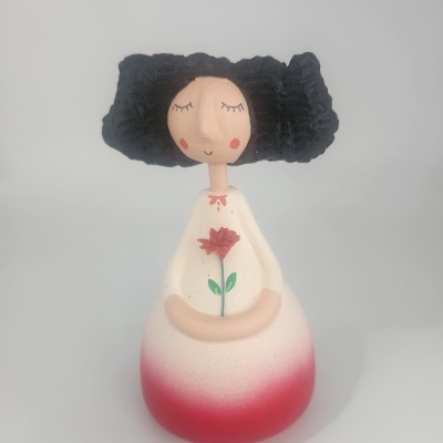 Boneca decorativa de cerâmica com cabelo preto e vestido branco e vermelho com flor pintada.
