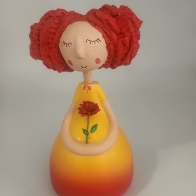 Figurinha decorativa de mulher com vestido amarelo e vermelho, cabelo vermelho e flor pintada
