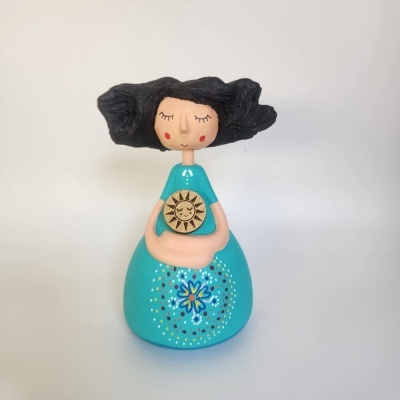 Boneca decorativa com cabelo preto e vestido azul com pintura floral e sol dourado.