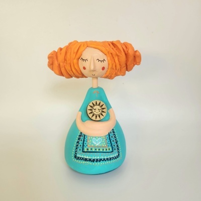 Boneca decorativa com cabelo laranja e vestido azul com símbolo de sol dourado