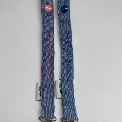 Dois suportes de chupeta azuis com texto 'I'm a girl' e 'I'm a boy'.