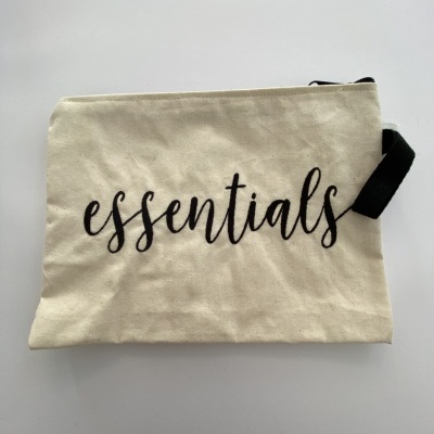 Necessaire bege com fecho preto e a palavra 'essentials' em letra cursiva negra