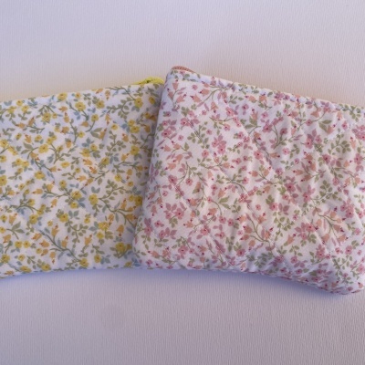 Duas bolsas acolchoadas com padrão floral, uma amarela e outra rosa, com etiqueta de flor.