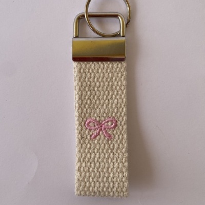 Porta-chaves de tecido cru com laço rosa bordado e metal prateado