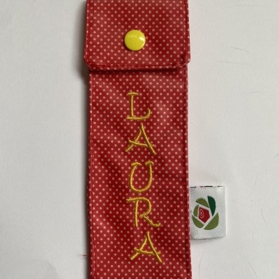 Estojo vermelho com pontos brancos e nome Laura bordado amarelo.