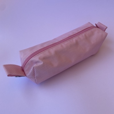Estojo retangular rosa com fecho de correr e padrão de pontos brancos.