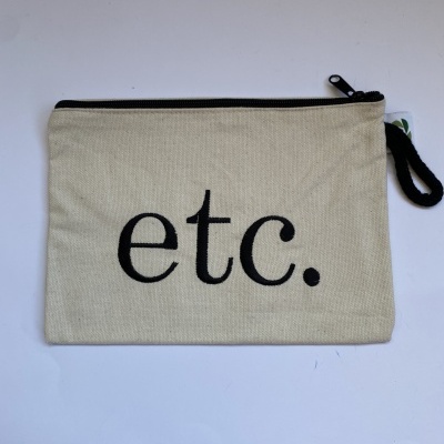 Bolsa pequena em tecido cru com fecho preto e a palavra 'etc.' em letras pretas