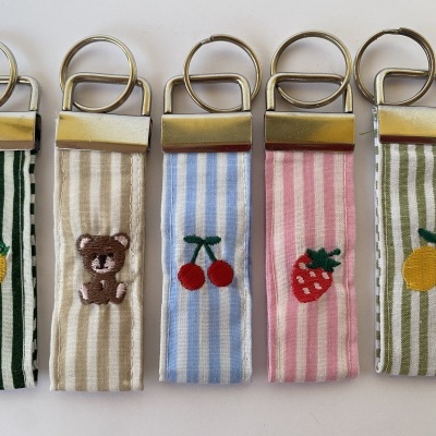 Cinco porta-chaves de tecido riscado com bordados de frutas e urso.