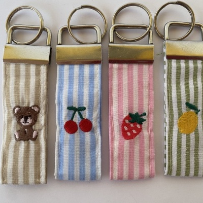 Porta-chaves de tecido riscado com bordados e argolas de metal.