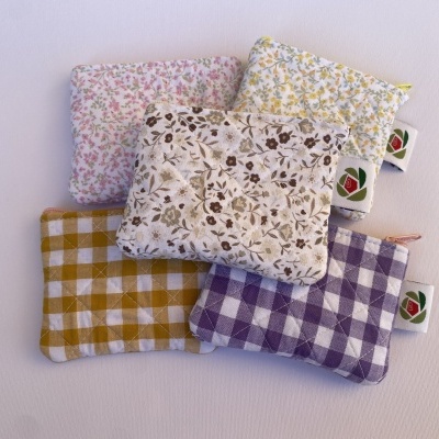 Cinco bolsas pequenas de tecido com padrões florais e xadrez em várias cores sobre fundo branco.