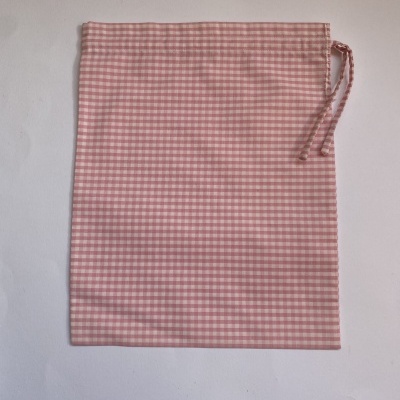 Saco de tecido rosa e branco com padrão de quadrados e cordão na parte superior direita