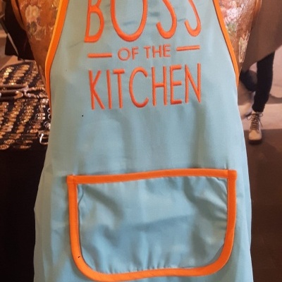 Avental azul claro com texto laranja BOSS OF THE KITCHEN