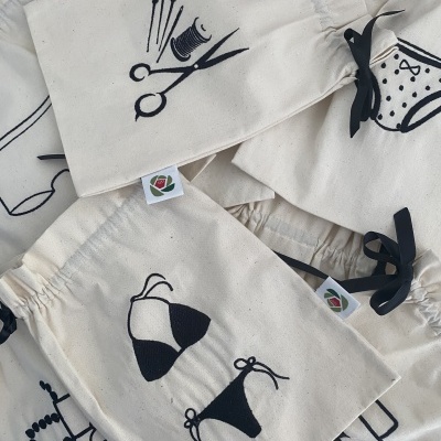 Sacos de algodão cru com estampas pretas de tesouras, linha, agulhas, biquíni, meias, colar e mala.