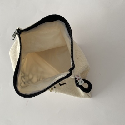 Saco pequeno branco de tecido com fecho preto aberto mostrando o interior.