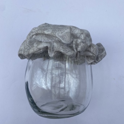 Frasco de vidro com tampa de tecido cinzento e padrão branco