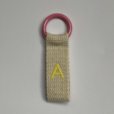 Porta-chaves de tecido bege com letra A amarela e argola cor-de-rosa