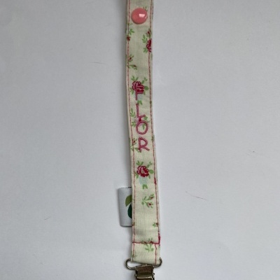 Presilha para chupeta branca com padrão floral e texto FLOR bordado
