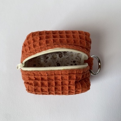 Estojo castanho-avermelhado com fecho éclair creme aberto, argola metálica e forro floral