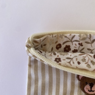 Bolsa de tecido às riscas bege e branco com bordado de urso e interior floral.