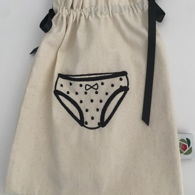 Saco de tecido cru com cordão preto e ilustração de roupa interior em preto.