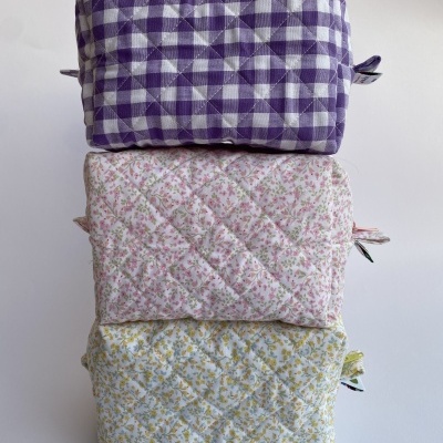 Três necessaires acolchoadas empilhadas com padrões xadrez e florais coloridos.