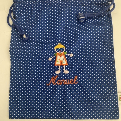 Saco azul com bolinhas brancas e bordado de boneco com nome 'Manuel'.