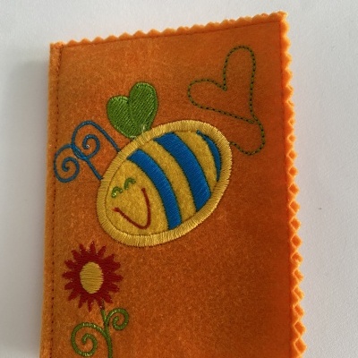 Capa de tecido laranja com bordados coloridos de abelha, coração e flor