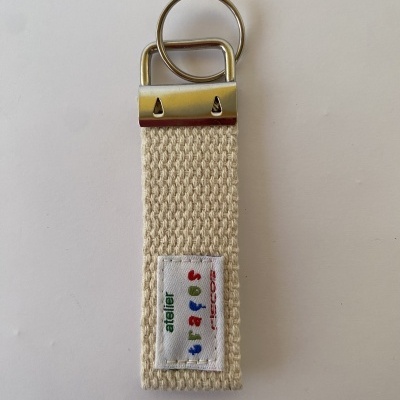 Chaveiro de tecido bege com argolas metálicas e etiqueta colorida