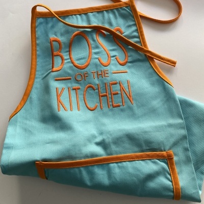 Avental azul claro com bordas laranja e texto BOSS OF THE KITCHEN