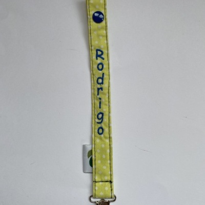 Prendedor de chupeta amarelo com nome Rodrigo bordado em azul.