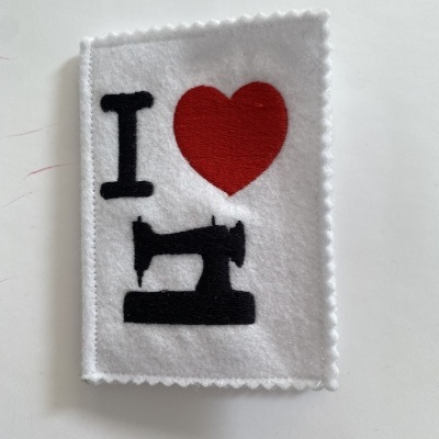 Tecido branco com bordas serrilhadas e desenho bordado 'I (coração) máquina de costura'