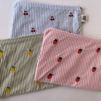 Três bolsas de tecido às riscas com bordados de frutas e fecho zip.