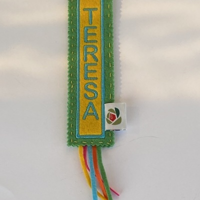 Marcador de livros artesanal verde e amarelo com o nome TERESA bordado e fitas coloridas.