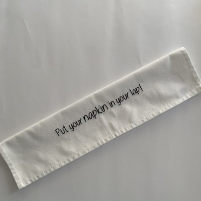 Guardanapo de tecido branco com texto preto colocado sobre superfície branca