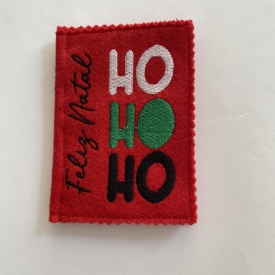 Etiqueta de tecido vermelho com texto bordado HO HO HO e Feliz Natal.