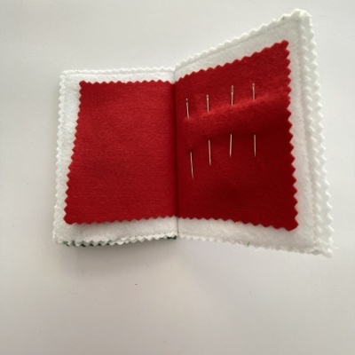Estojo pequeno aberto com agulhas em feltro vermelho e bordas brancas