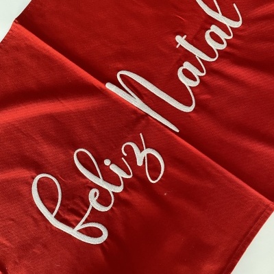 Tecido vermelho com bordado branco a dizer feliz Natal